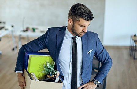 Mann im Anzug verlässt das Büro mit einem Karton persönlicher Sachen