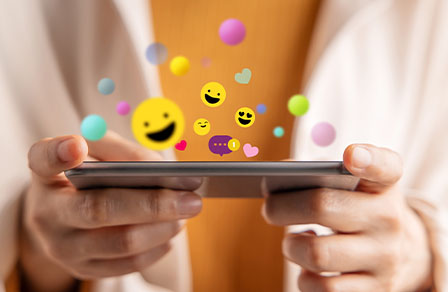 Smartphone en main, smileys et bulles de discussion au-dessus de l’écran