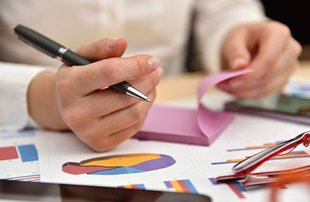 Hand mit Stift über ausgedruckten Diagrammen und rosa Haftnotizen