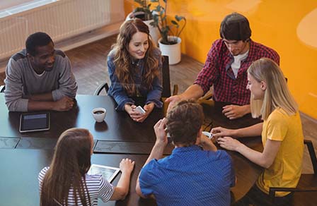 Seis jóvenes sentados a una mesa con tabletas conversan