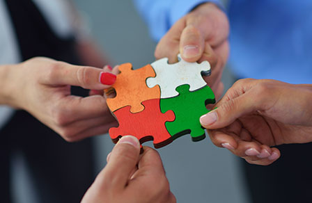 Hände mehrerer Menschen fügen vier bunte Puzzleteile zusammen