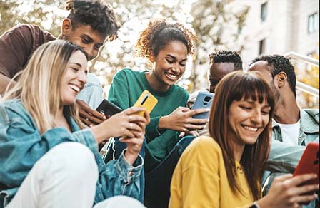 Un grupo de jóvenes sentados en la calle se ríe mirando el teléfono